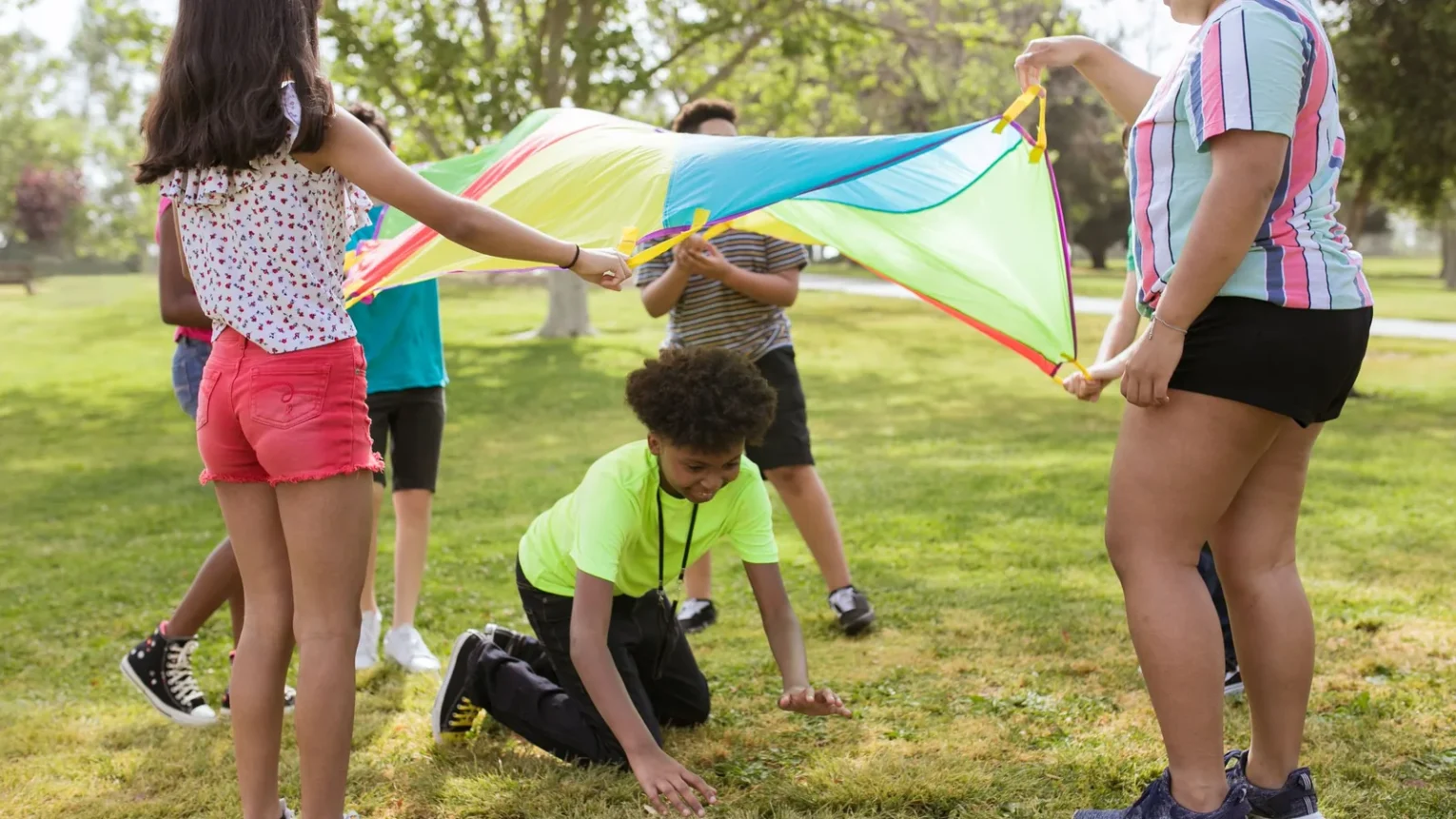 Children playing with a colorful parachute outdoors at an Indian River County summer camp