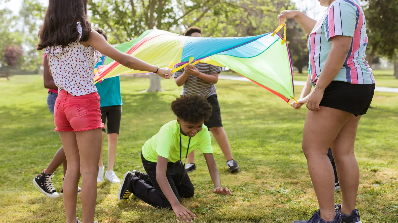 Children playing with a colorful parachute outdoors at an Indian River County summer camp